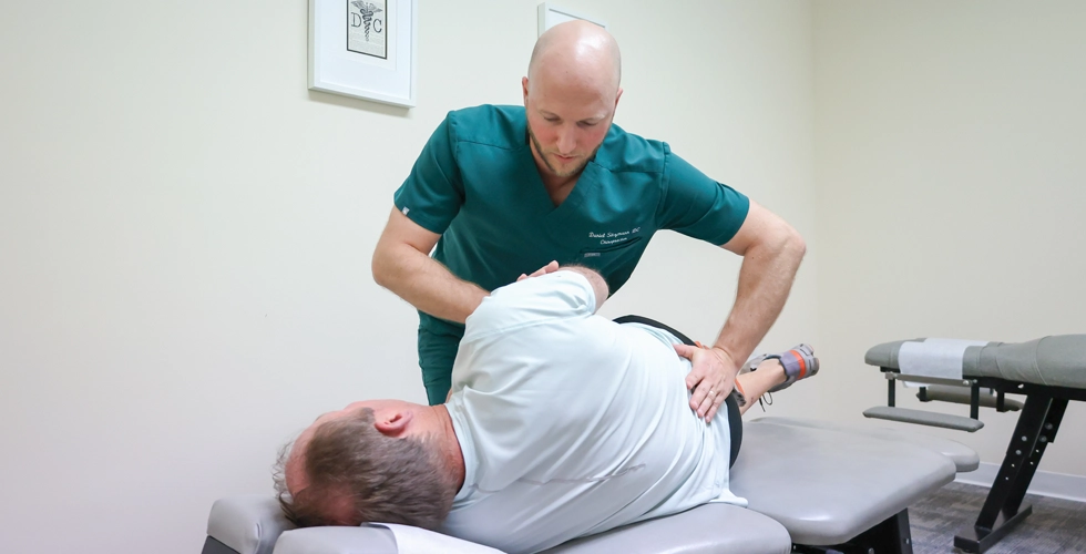Chiropractor performing spinal adjustment on patient lying on table
