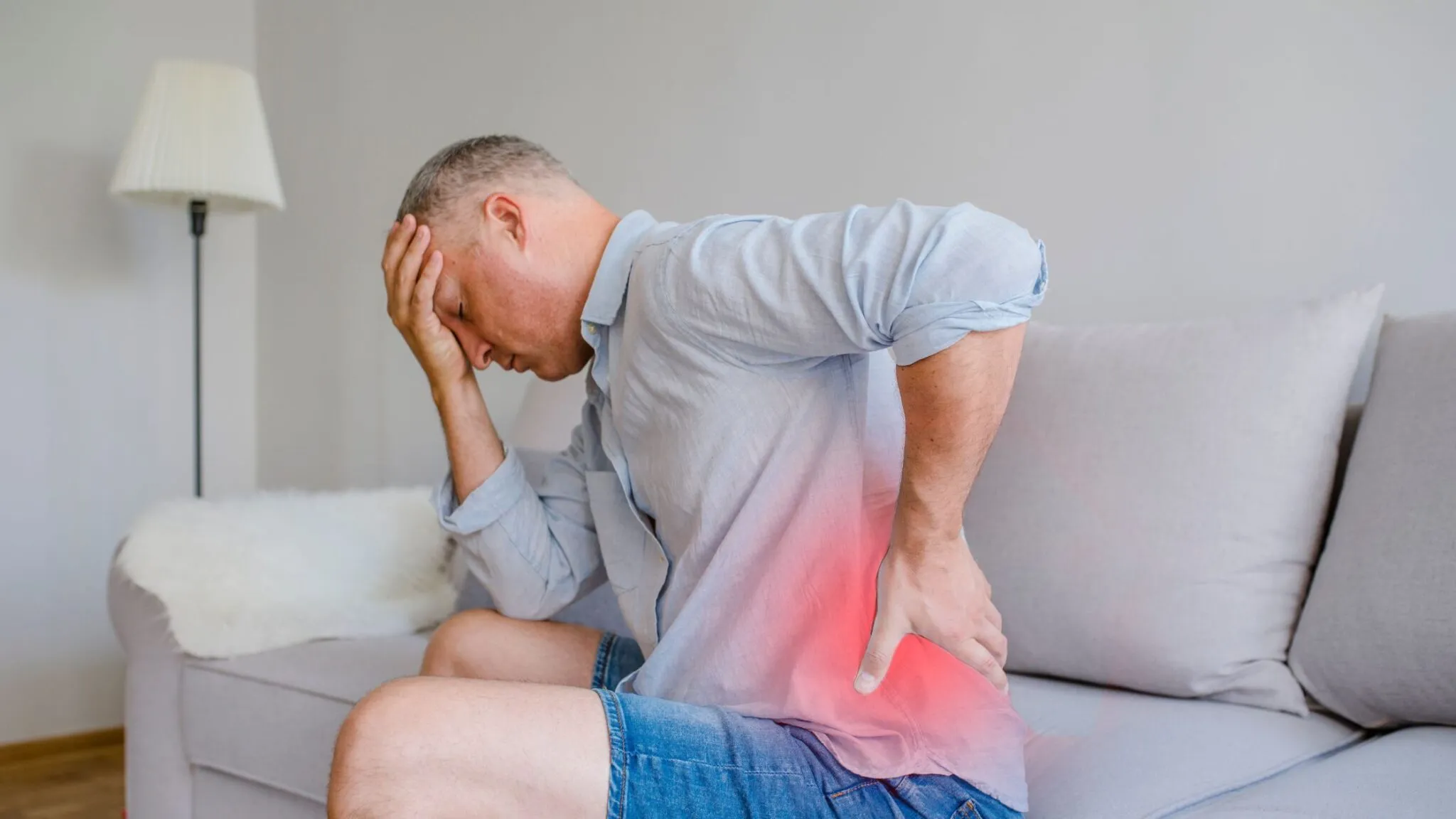 Man experiencing severe lower back pain while seated at home, indicating need for back pain treatment