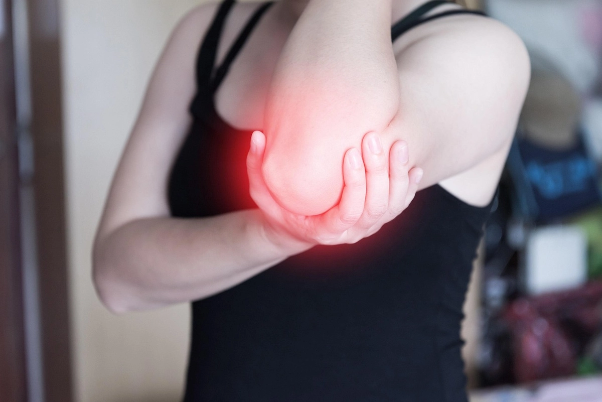 Woman holding her elbow in distress due to sharp joint pain and inflammation, highlighting a need for treatment.