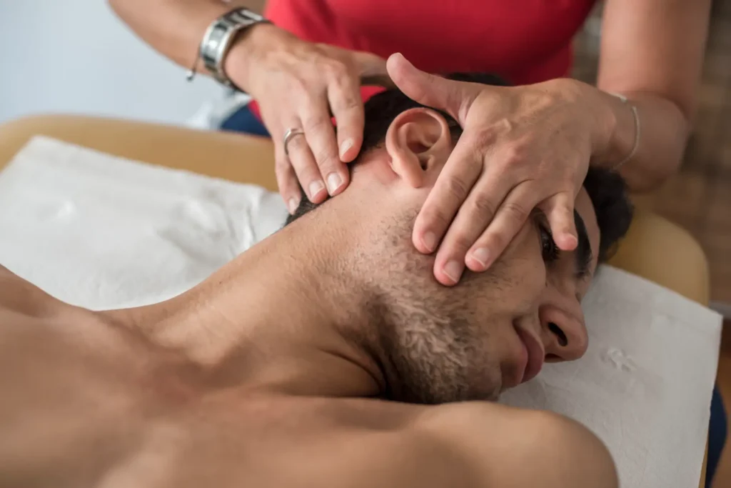 Close-up of a person receiving a head and neck massage from a therapist, lying on a massage table.