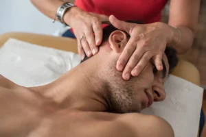 Close-up of a person receiving a head and neck massage from a therapist, lying on a massage table.