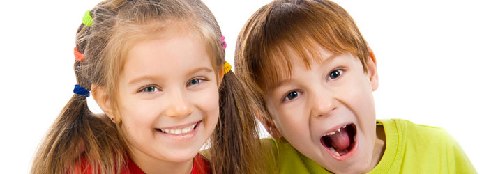 A young girl smiling broadly next to a young boy with his mouth open wide in a playful shout, both against a white background.